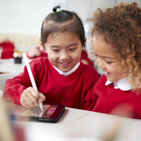 Close up of two kindergarten schoolgirls using a tablet computer and stylus
